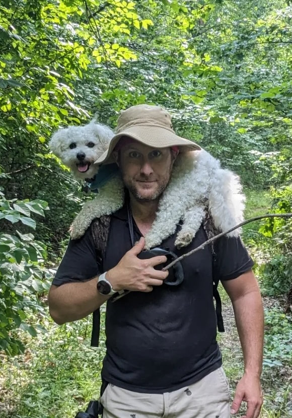 Jarrod hiking on the Sheltowee Trace Trail with his white fluffy bichon frise, Lucky